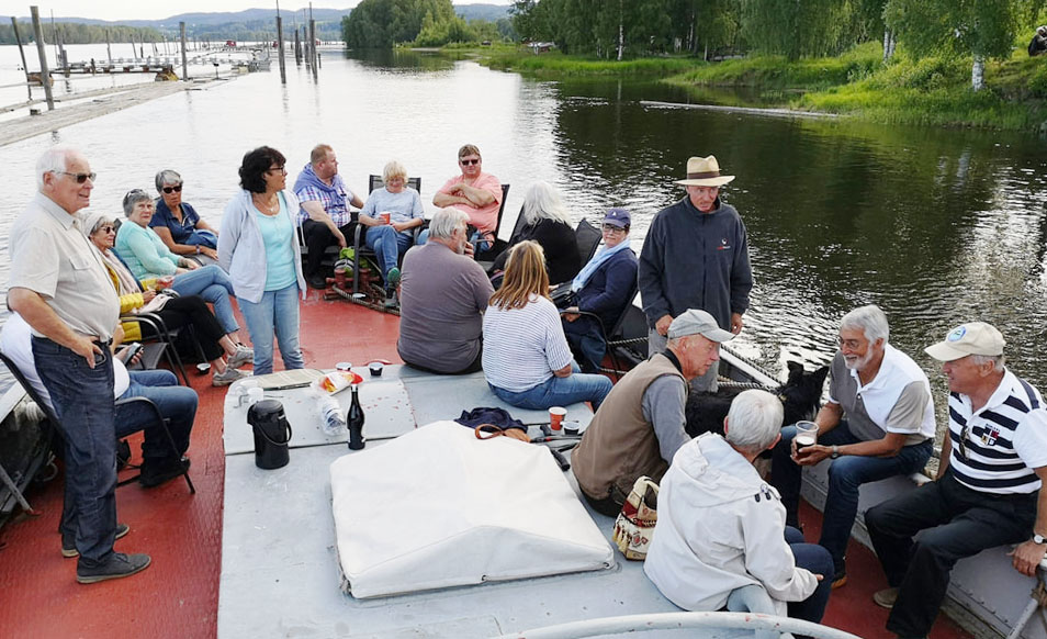Foto av mennesker som står og sitter på akterdekket på båten.